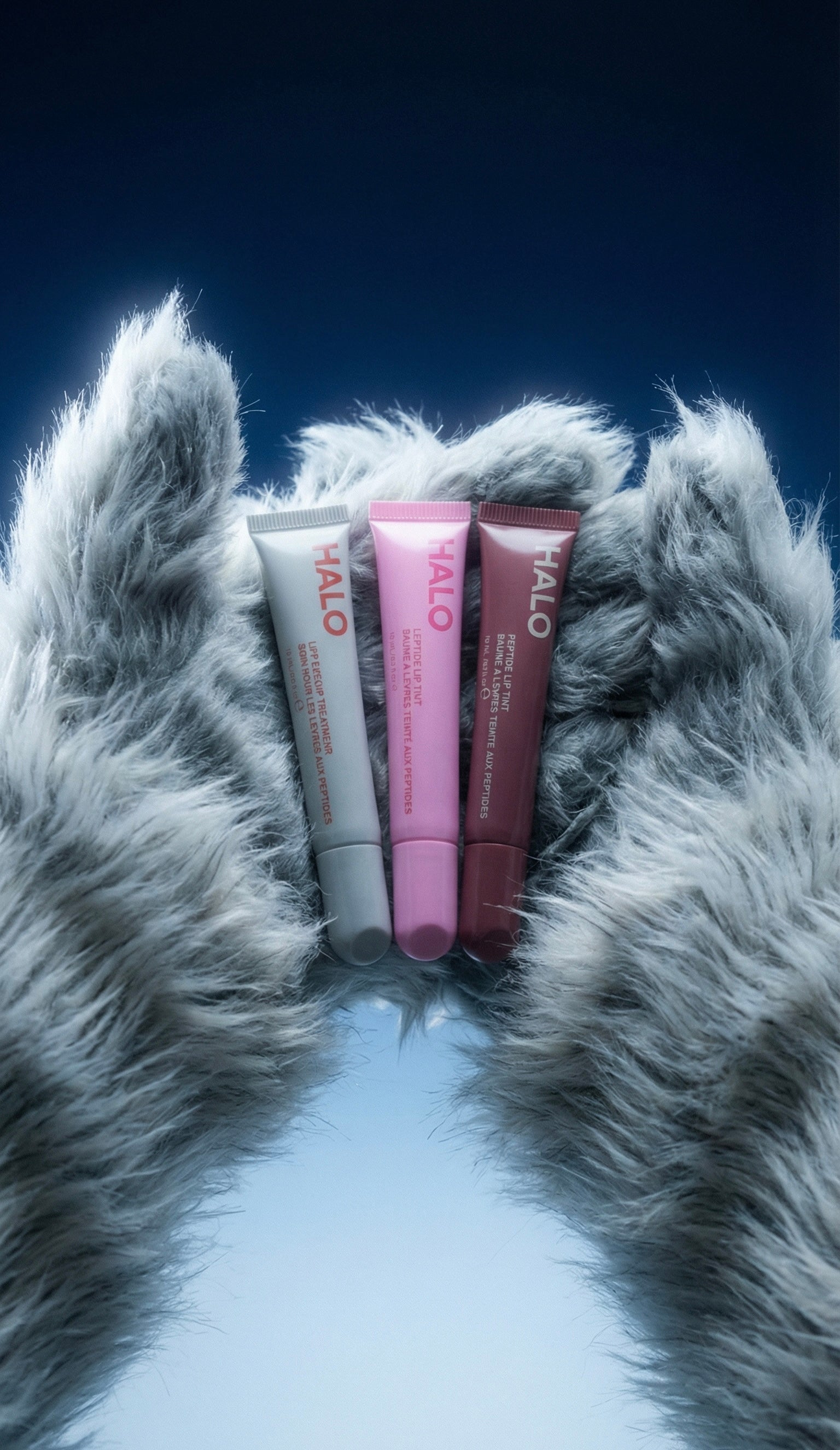 Three tubes of Halo lip balm on a fluffy gray surface with a blue gradient background